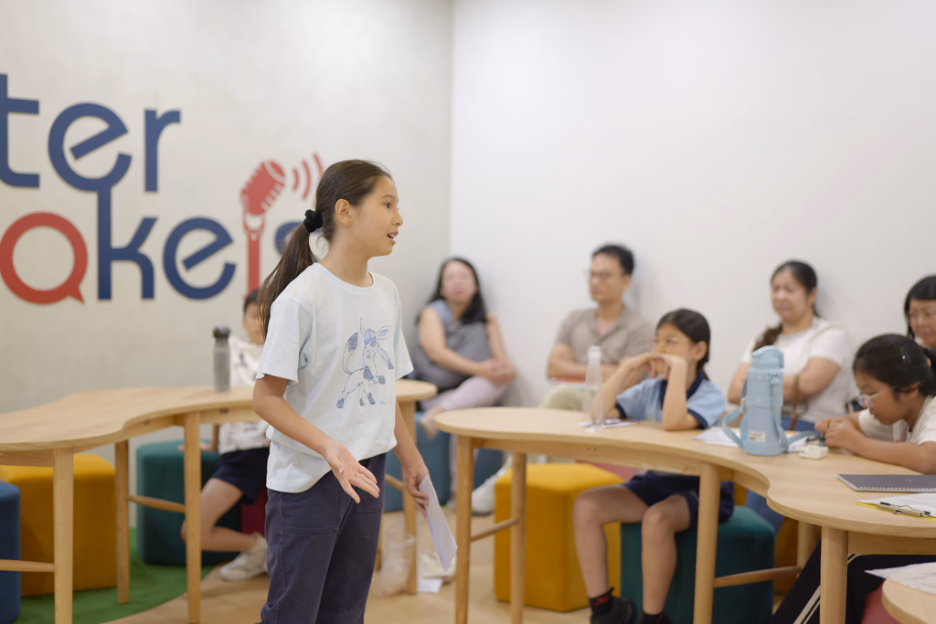 Primary student presenting an idea to classmates around tables